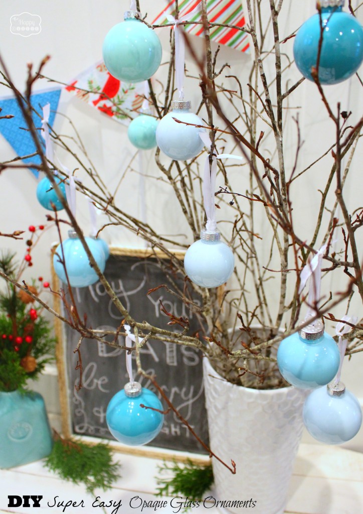The blue, white and green ornaments hanging from a twig tree that is in a white vase.