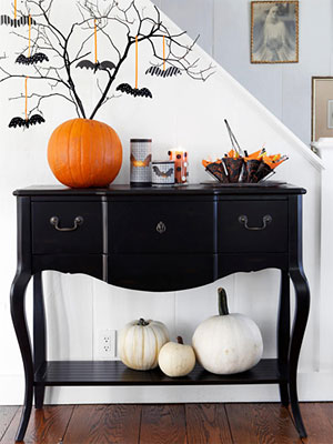 A black entryway table with an orange pumpkin tree on top and bats on the branches.