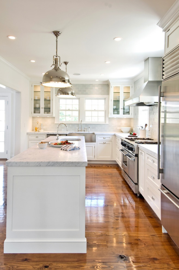 Wooden floors and a white island with stainless steel lights above the island in the kitchen.