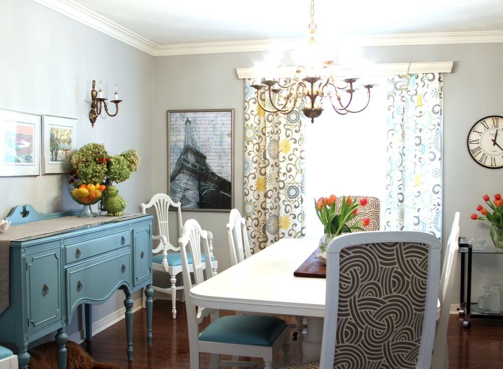 A living room with a white table, tulips in the center of the table and a chandelier over top.