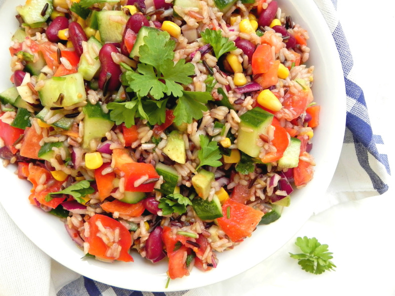 Colorful-Chopped-Rice-Salad in a white bowl on a blue and white checkered tablecloth.