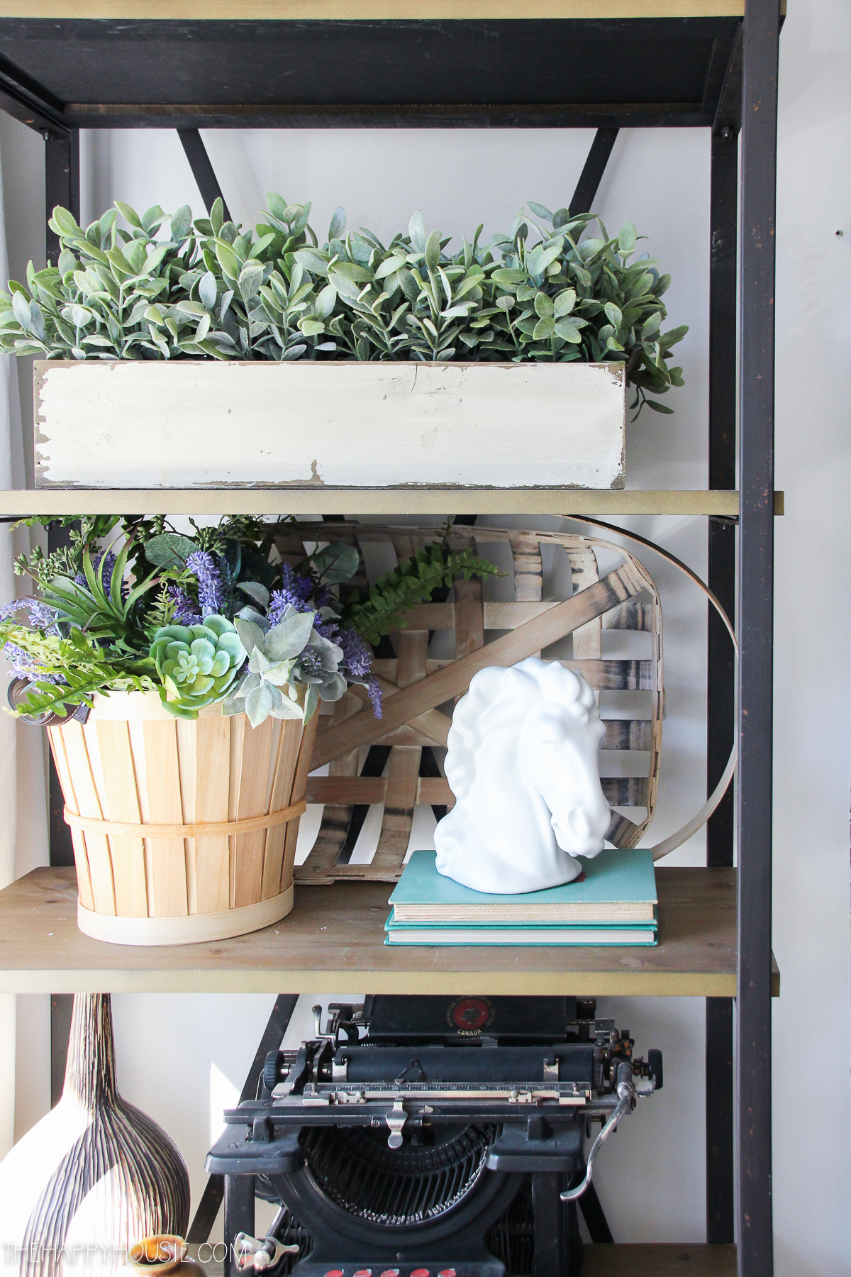 There is open shelving with plants and an antique typewriter on the shelves.